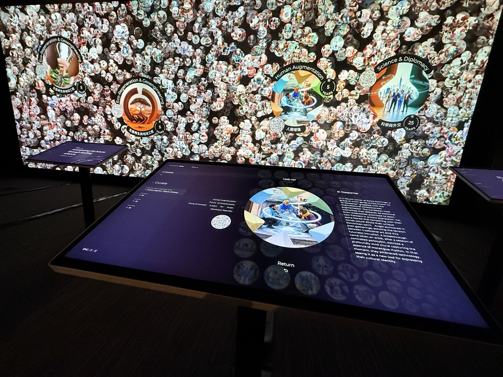 Interactive table screen showing a vision, with the projected wall of circular visions behind it naming Human Augmentation, Science and Diplomacy, and Eco-Regeneration and Geoengineering.