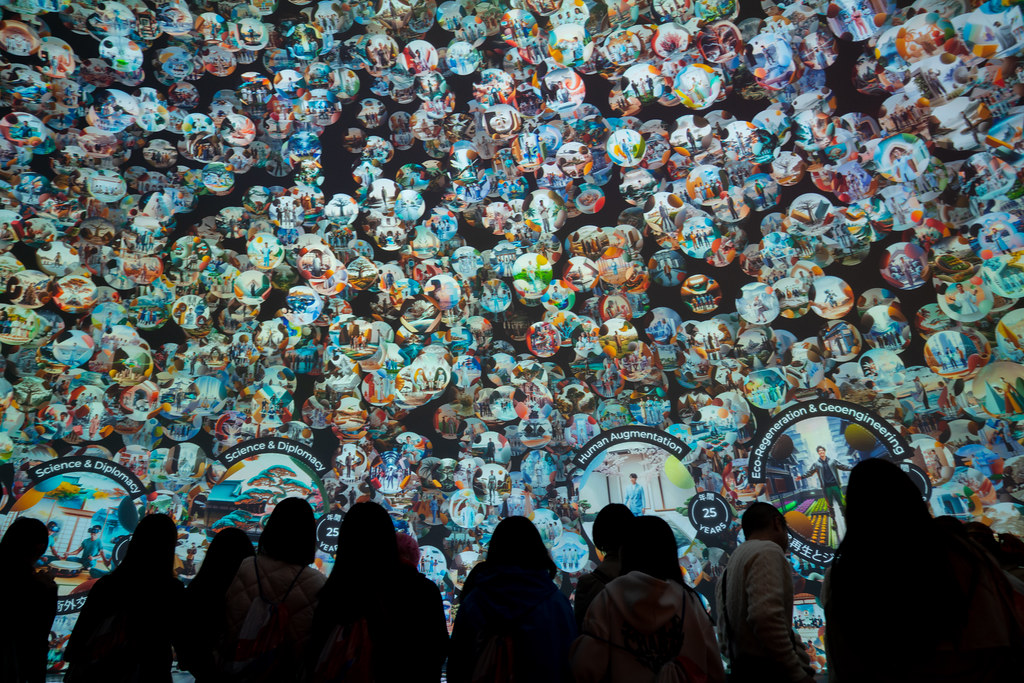 Silhouettes of a group of visitors in front of the wall of circular visions, with rings naming Science and Diplomacy, Human Augmentation, and Eco-Regeneration and Geoengineering.